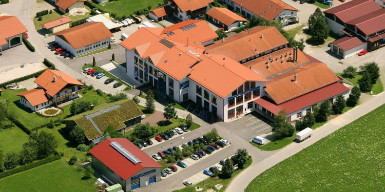 Luftaufnahme des Betriebsgeländes der Wäscherei Abel mit dem Hauptgebäude in der Mitte, den Nebengebäuden, wie die LKW-Silberhalle und die Werkstatt, und der Mitarbeiterparkplatz.